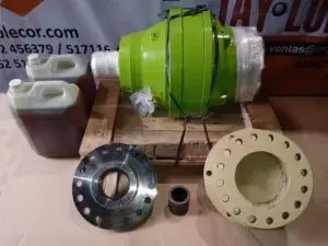 Conjunto de repuestos y componentes mecánicos incluyendo bomba hidráulica verde, bridas metálicas, sellos y piezas de recambio dispuestas sobre mesa de trabajo