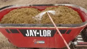 Mezcladora de alimento Jay-Lor de color rojo cargada con forraje picado, vista desde arriba mostrando el contenido y el mecanismo mezclador interno.